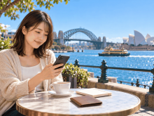 シドニーのカフェで海外送金アプリを確認するオーストラリア留学中の女性
